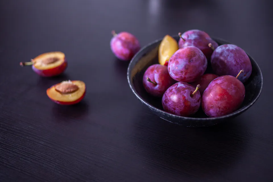 Fresh plums, whole and halved, on a dark surface, ready for pálinka production.