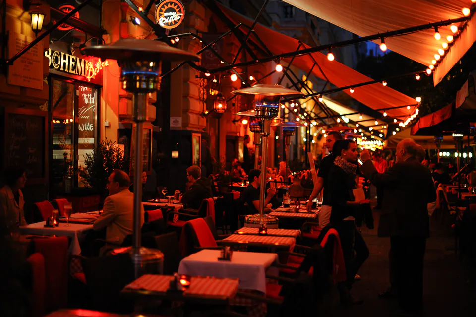 Evening restaurant terrace with string lights, outdoor tables, and diners enjoying the ambiance