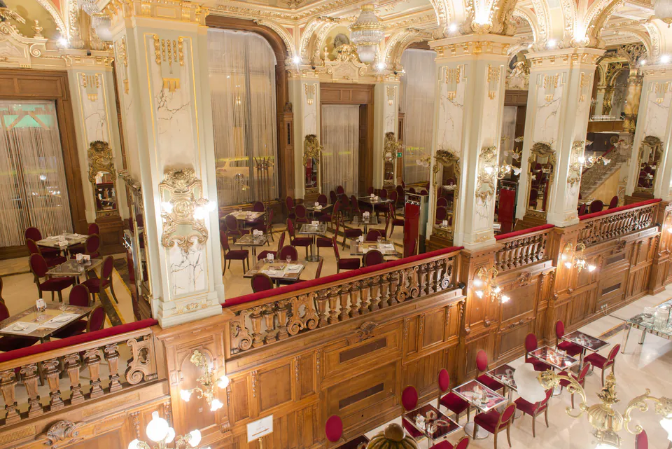 Ornate historic café interior with gilded mirrors, chandeliers and red velvet seating