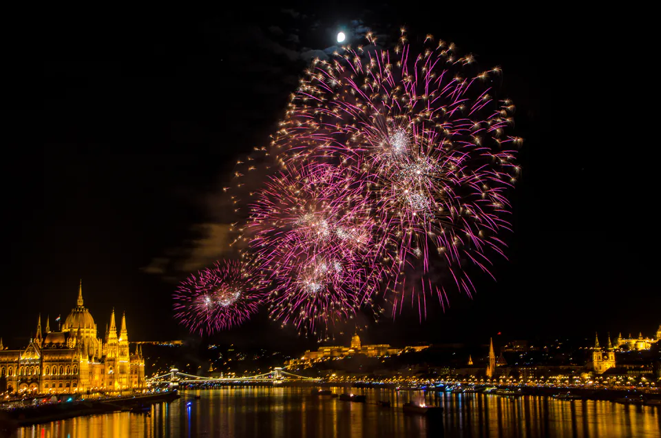 Pink and gold fireworks exploding over illuminated Budapest landmarks along the Danube River at night