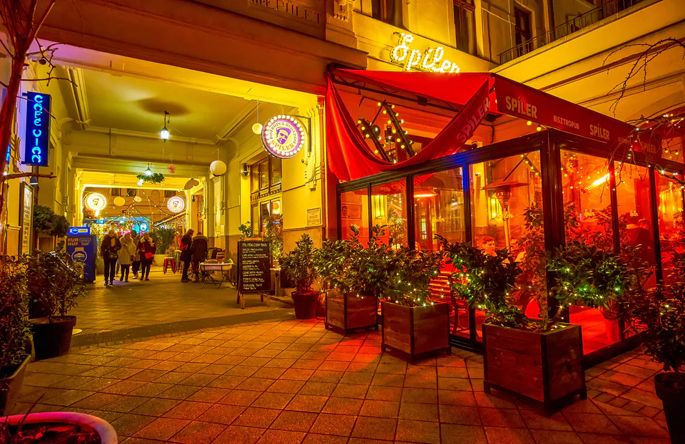 Illuminated restaurant entrance with red awning and string lights along a covered walkway at night