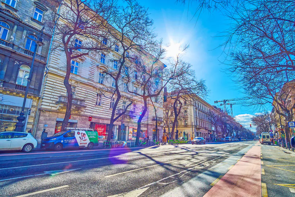 Tree-lined Andrássy Avenue with historic buildings and modern street life on a sunny day