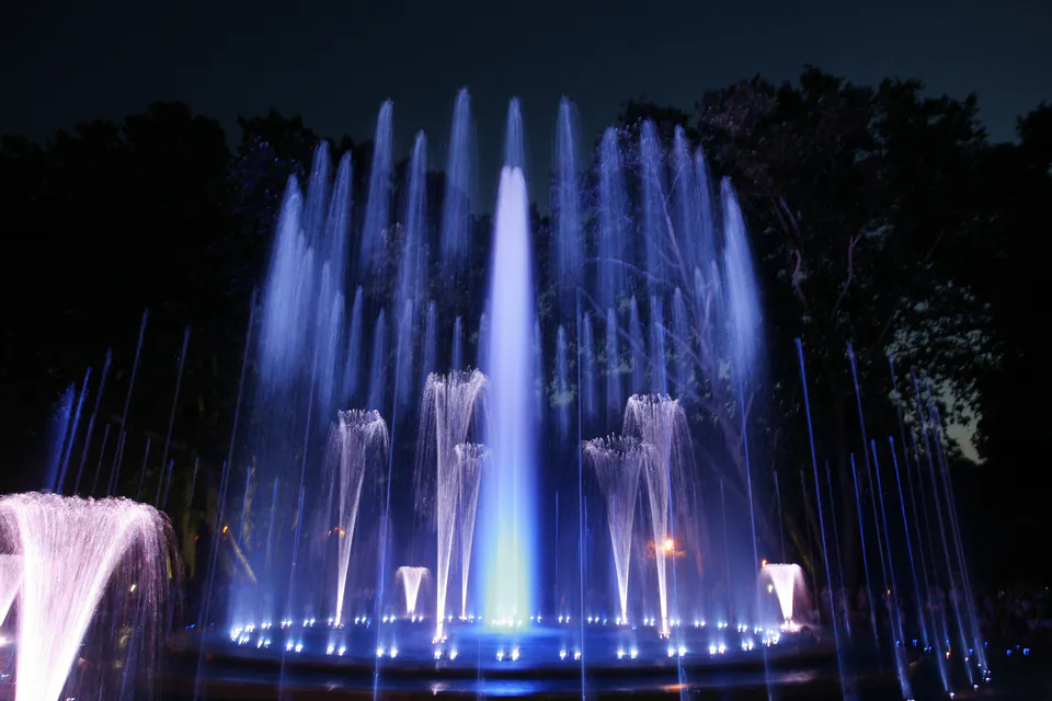 Illuminated musical fountain with blue and white water jets dancing against dark night sky