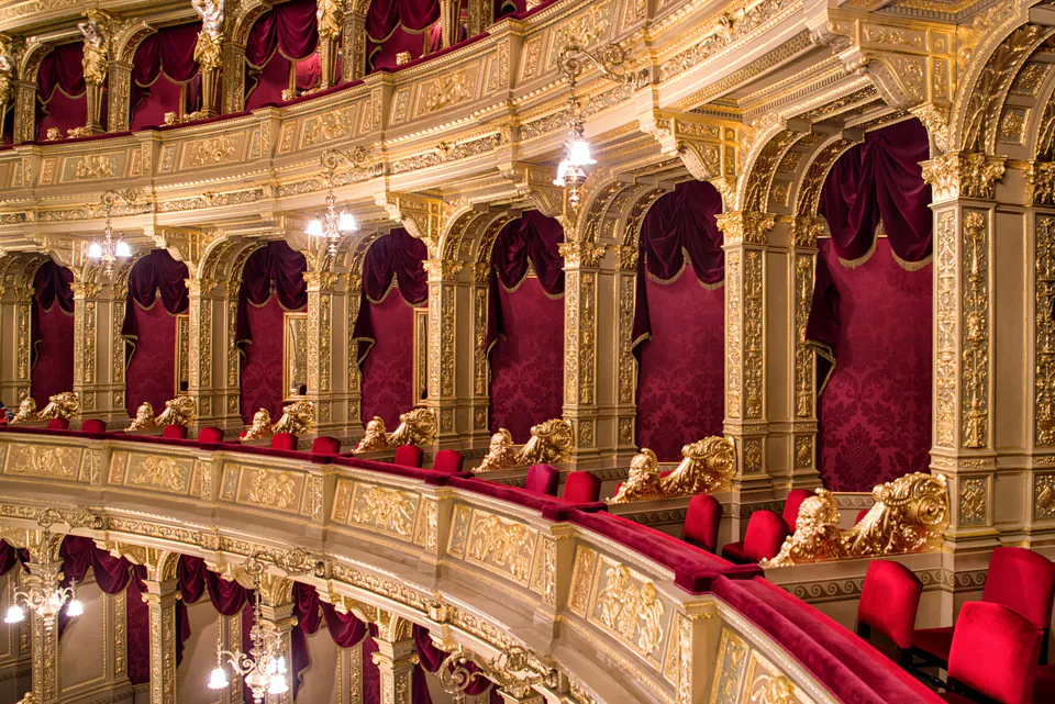 Ornate gilded balconies with red velvet seating inside historic opera house theater