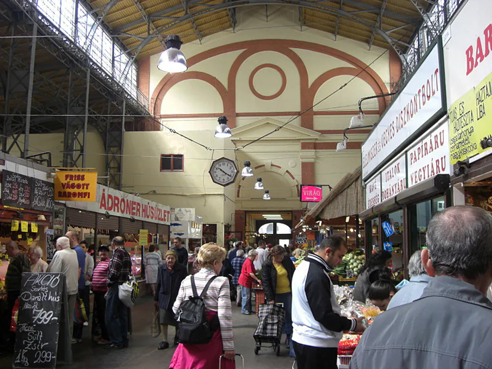 Interior of small covered market hall with vaulted ceiling and shoppers browsing vendor stalls