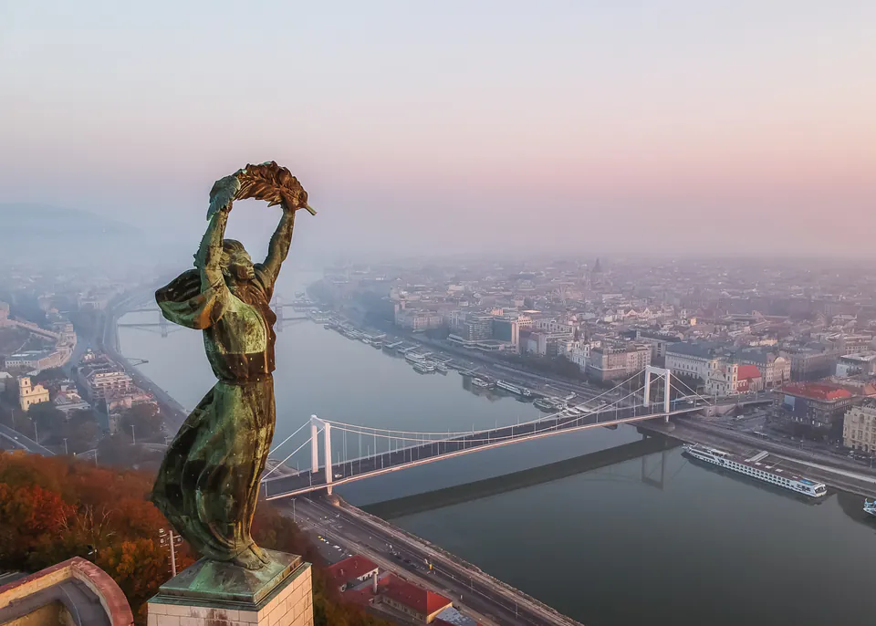 Liberty Statue overlooking Budapest with Danube River and bridges in background at sunset