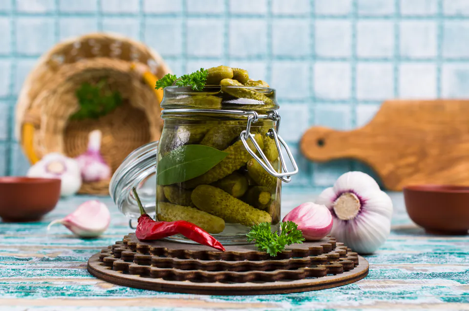 Glass jar of pickled cucumbers with garlic and spices on rustic wooden surface