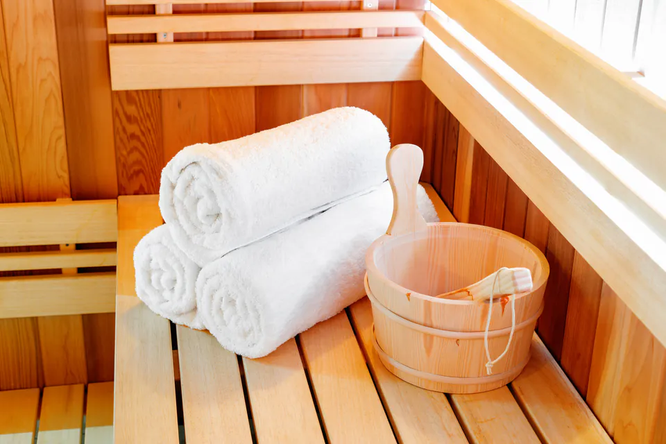 Clean white towels rolled neatly beside wooden bucket in traditional sauna