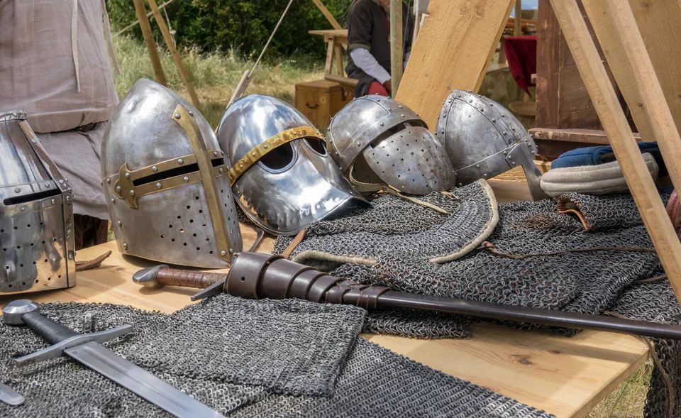Medieval helmets, chainmail armor and weapons displayed on wooden table