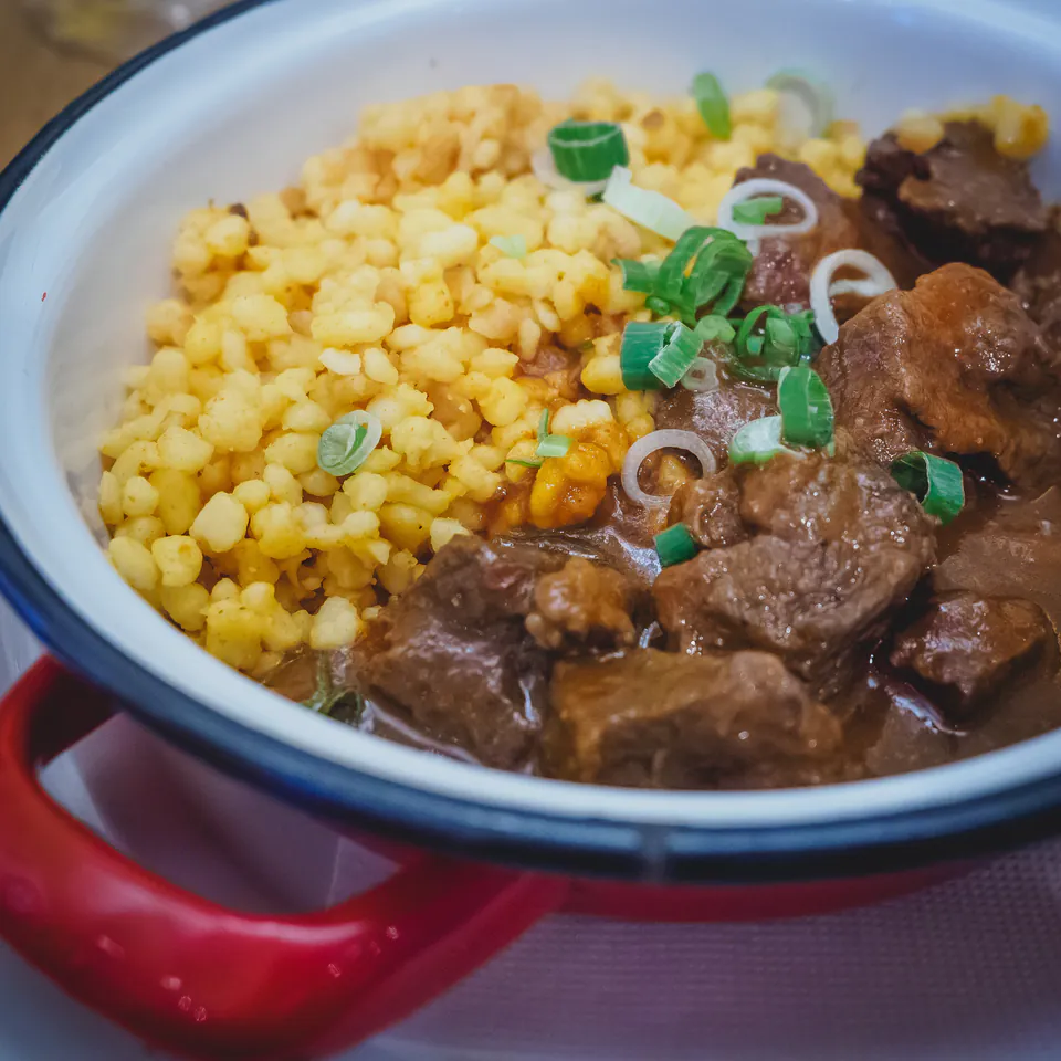 Traditional Hungarian beef stew served with yellow spätzle dumplings and green onions