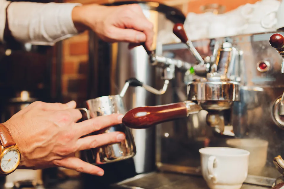 Close-up of hands operating professional espresso machine in café setting