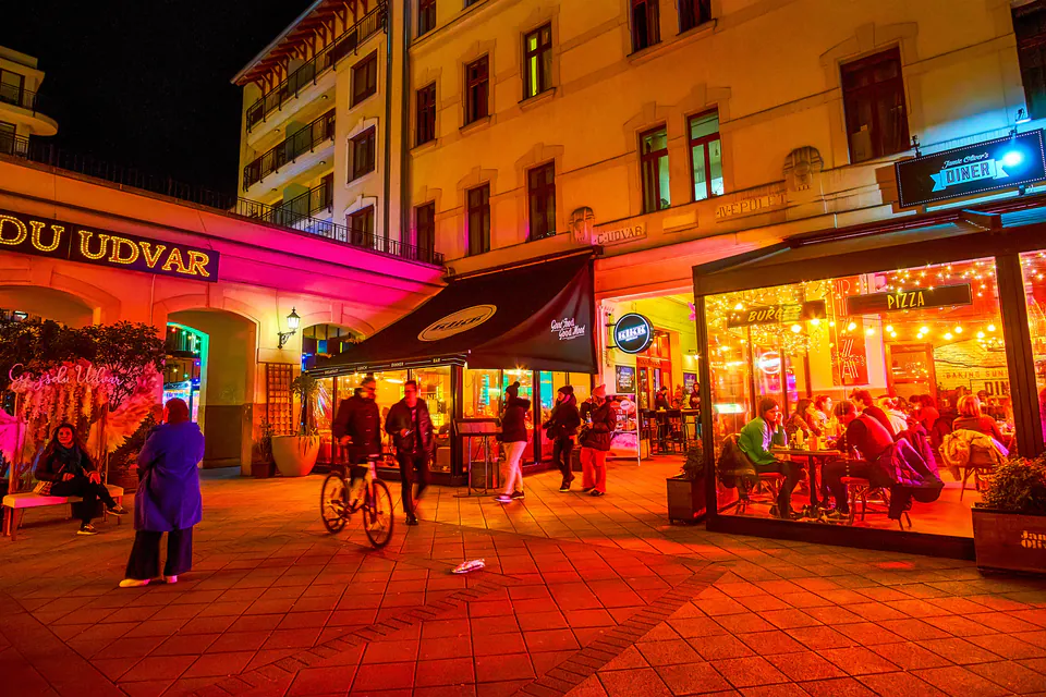 Lively nighttime scene at Gozsdu Udvar with illuminated restaurants and people walking through passageway