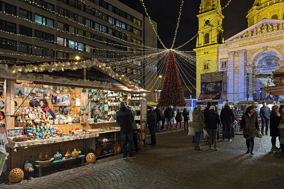 Festive Christmas market stalls with holiday decorations and shoppers at night in front of St. Stephen's Basilica, Budapest