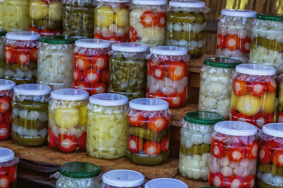 Rows of glass jars filled with colorful pickled vegetables including peppers, onions, and cucumbers