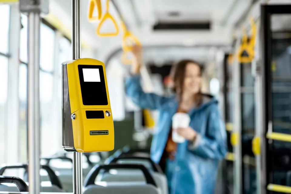 Yellow ticket validation machine mounted inside public transport vehicle with handrails visible