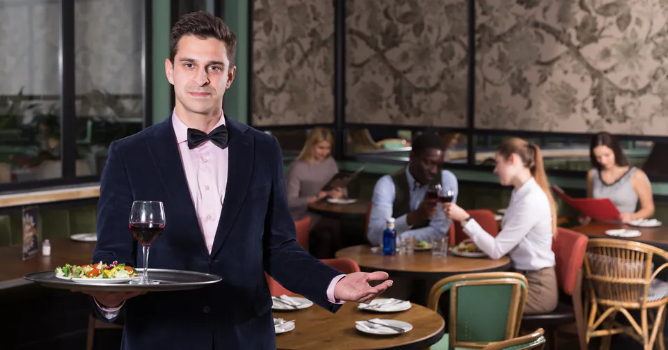 Professional server presenting food in an elegant restaurant dining room with customers seated in background