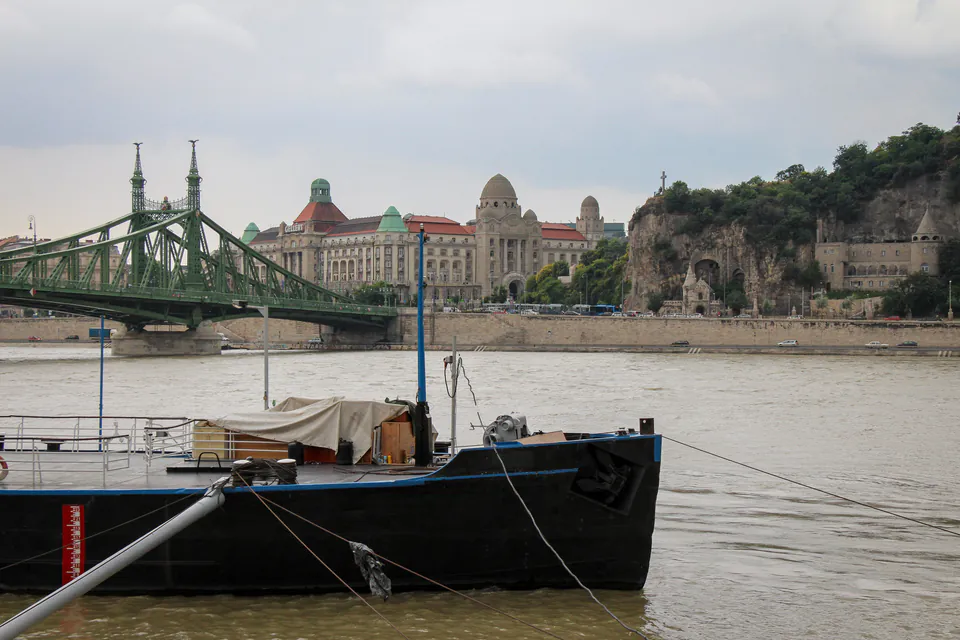View of Liberty Bridge and Gellért Hill with the Danube River and a moored boat in foreground