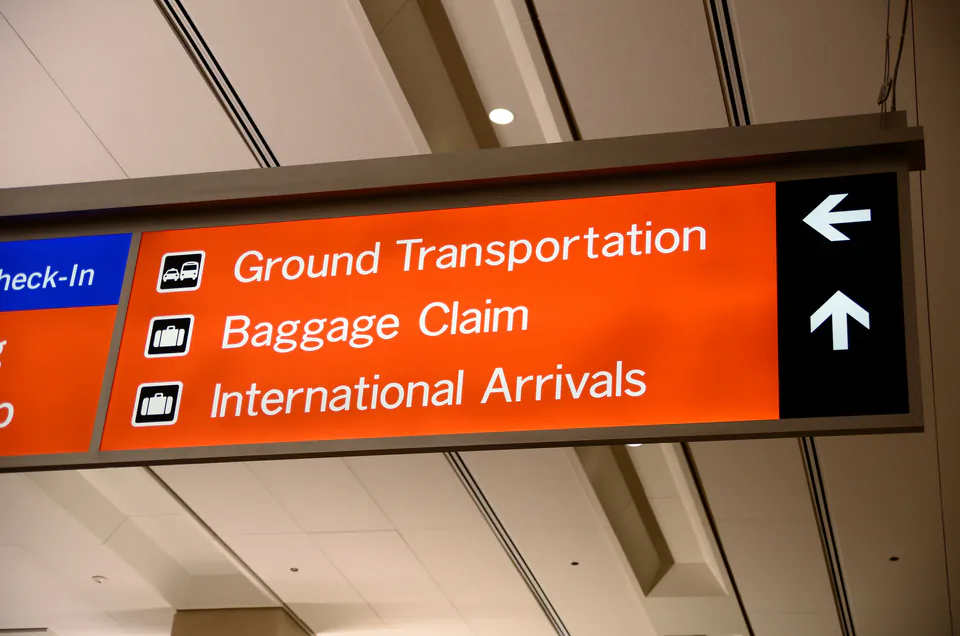 Orange airport directional sign showing Ground Transportation, Baggage Claim and International Arrivals