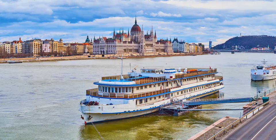 Multi-deck boat hotel moored on Danube River with Hungarian Parliament building in background
