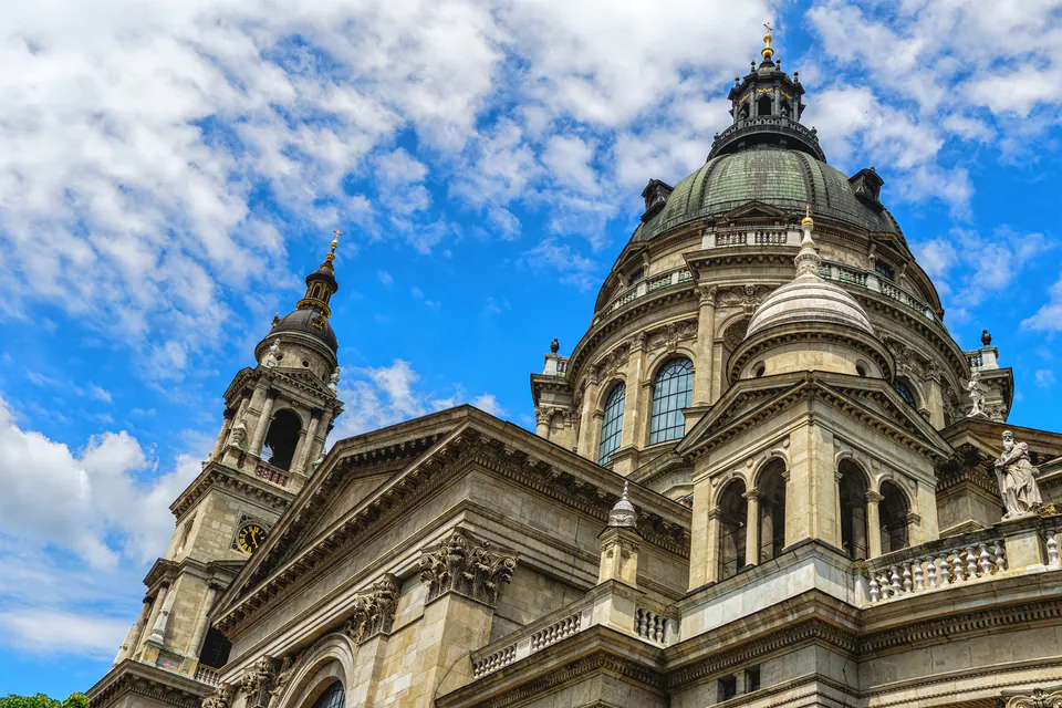 Ornate neoclassical dome and facade of St. Stephen's Basilica against blue sky with white clouds