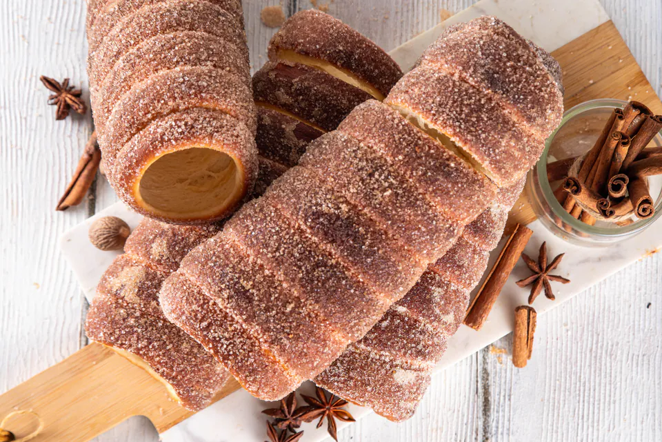 Fresh kürtőskalács pastries dusted with cinnamon sugar displayed with spices on wooden board