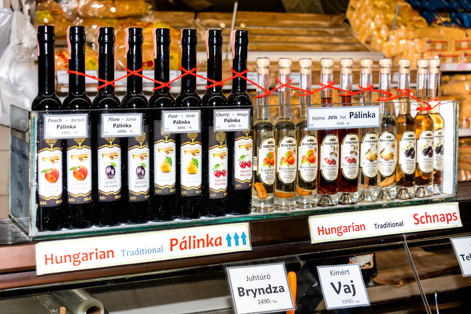 Display shelf of traditional Hungarian pálinka bottles with fruit labels and red ribbons