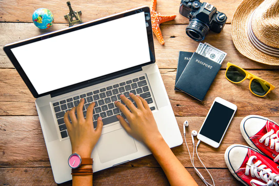 Person booking travel accommodations with laptop surrounded by travel items