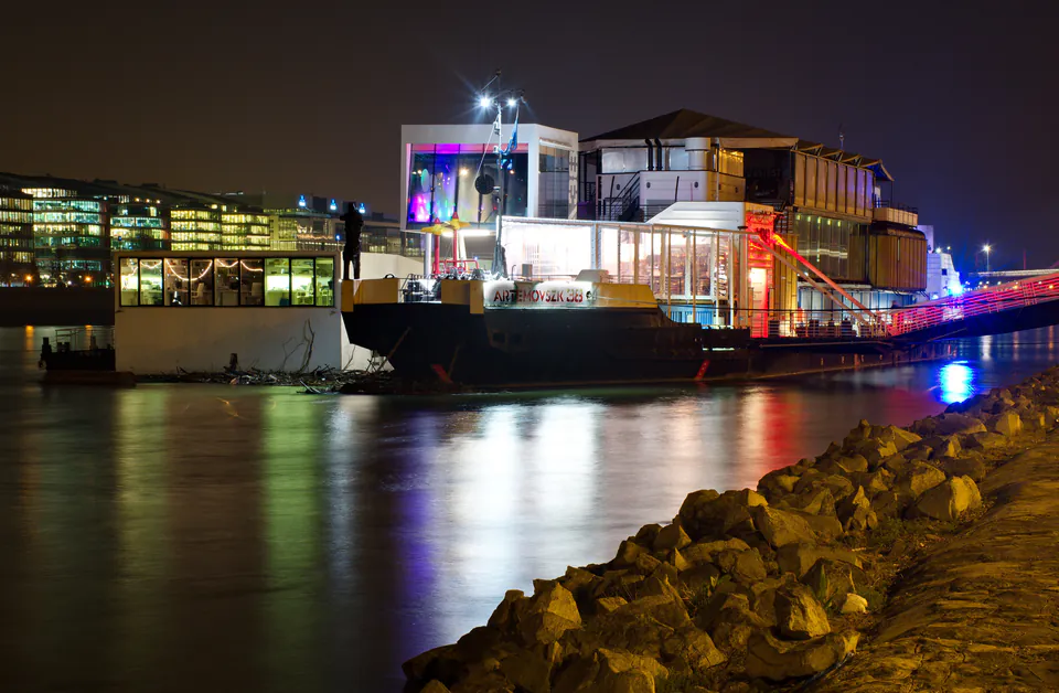 Illuminated A38 boat venue moored on Danube River at night with colorful reflections on water
