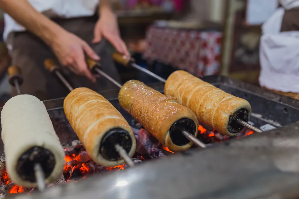 Fresh kürtőskalács pastries roasting on wooden spits over hot charcoal coals