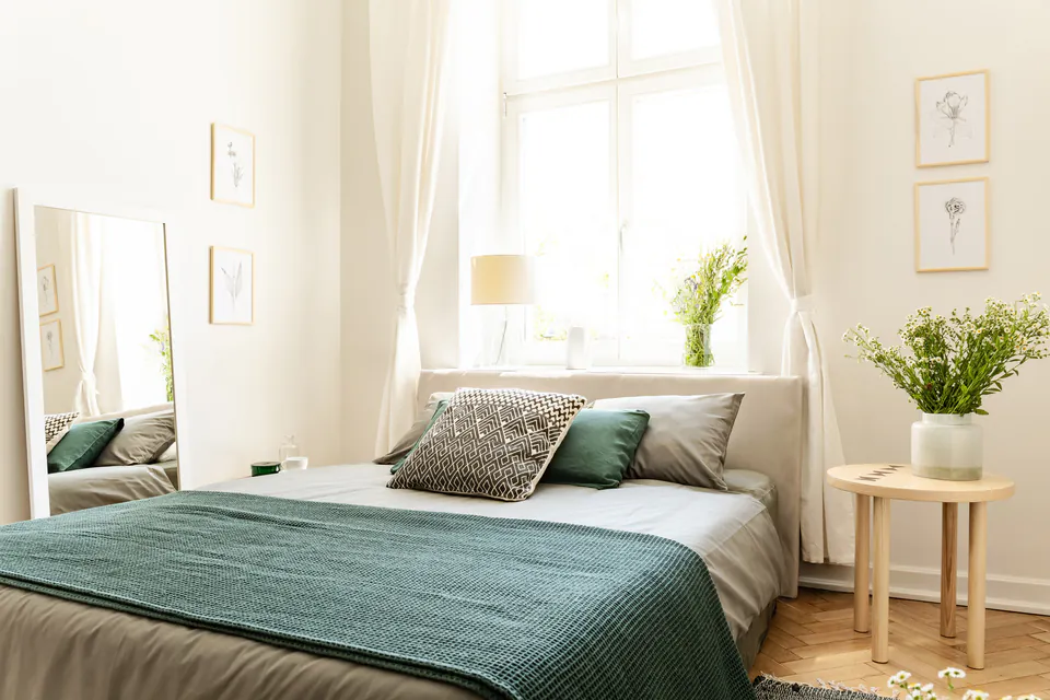 Bright guesthouse bedroom with green bedding, white curtains, and natural light