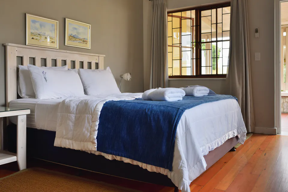 Modern guesthouse bedroom with white linens, blue throw blanket and wooden floors