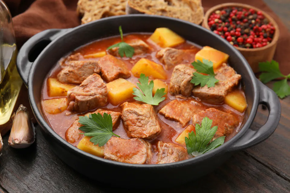Traditional Hungarian goulash with tender meat, potatoes and fresh herbs in black ceramic pot