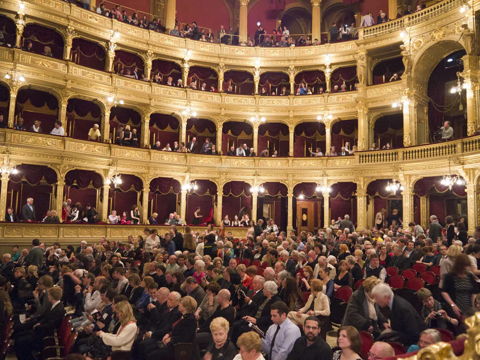 Interior of opera house showing ornate balconies filled with formally dressed audience members