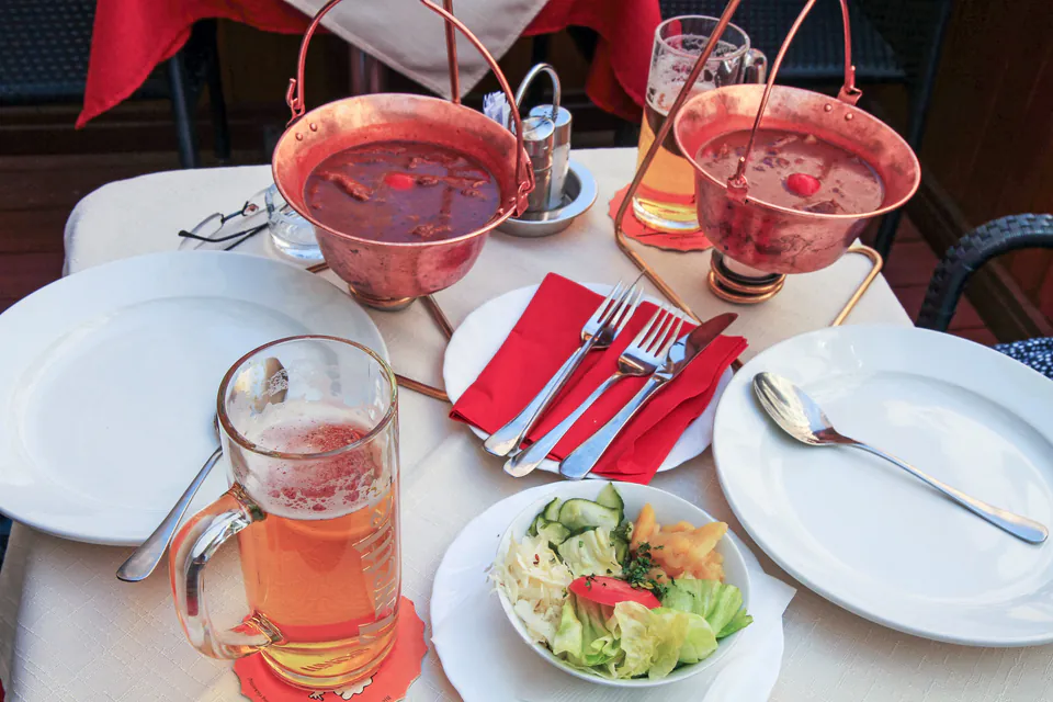 Elegant restaurant table with copper pots of goulash, beer, and salad.