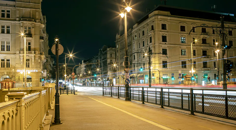Well-lit urban street at night with historic buildings and street lamps illuminating empty sidewalks