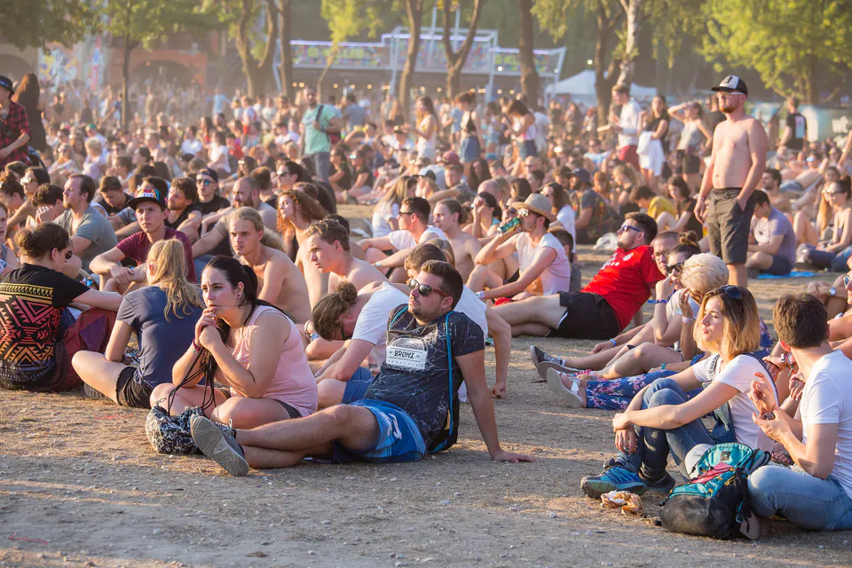 Large crowd of people sitting on the ground at an outdoor summer concert venue