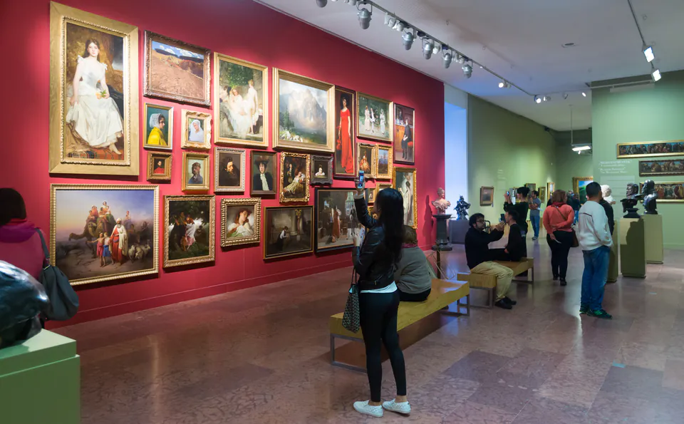 Museum visitors viewing portrait gallery with paintings on red and green walls
