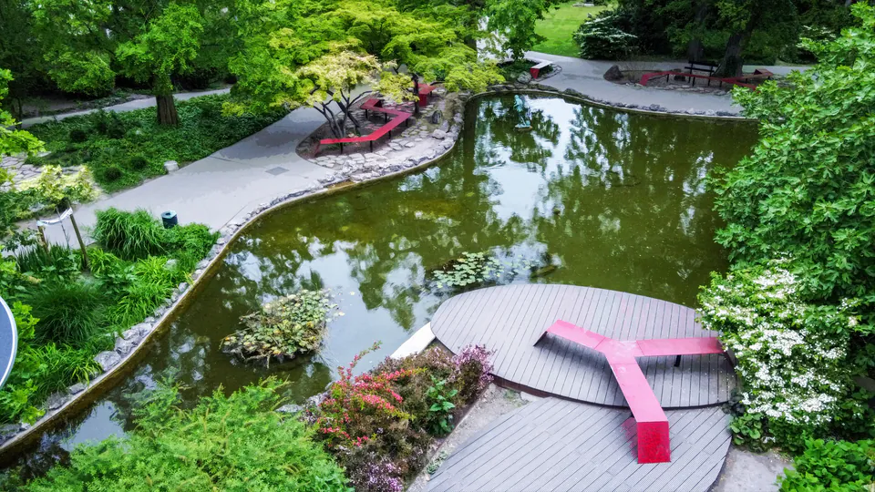 Tranquil Japanese garden with curved wooden platforms and decorative red elements over koi pond