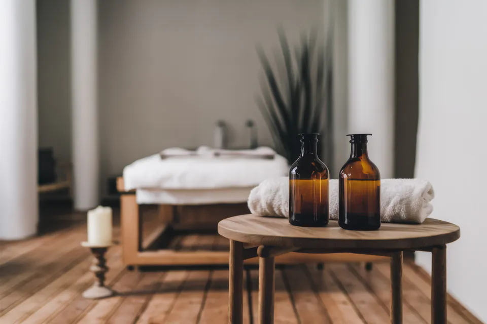 Minimalist spa treatment room with massage table, amber bottles and white towels