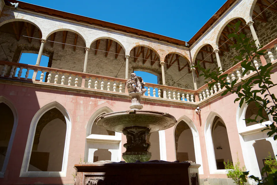 Renaissance courtyard with ornate fountain at center surrounded by arched colonnade and pink walls