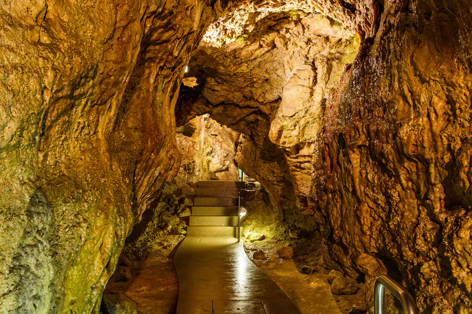 Illuminated stone passageway with stairs winding through natural cave tunnels beneath Buda Castle