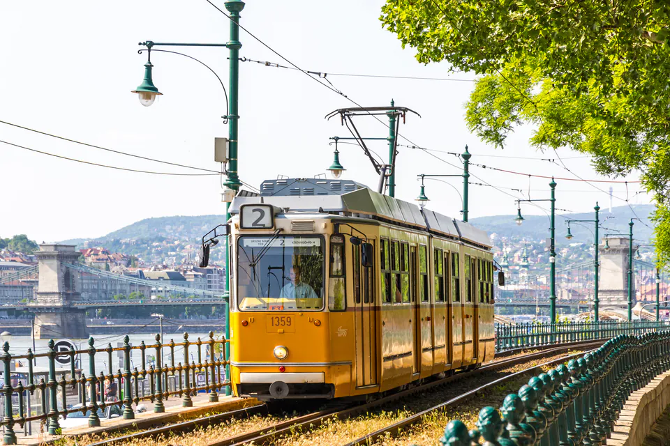 Yellow Budapest tram traveling along the Danube with Parliament building in background