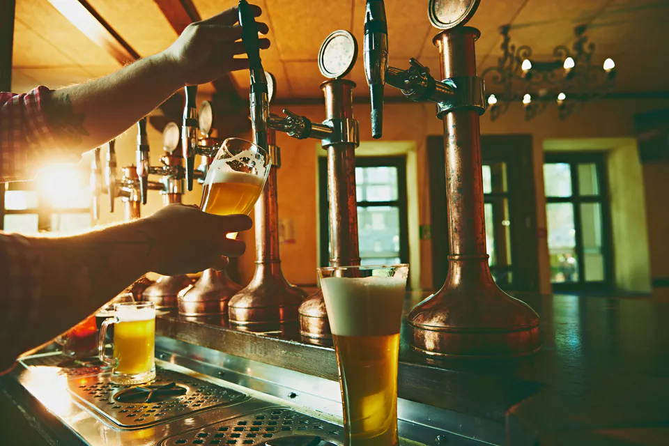 Bartender pouring draft beer from tap handles at bar counter in warm lighting