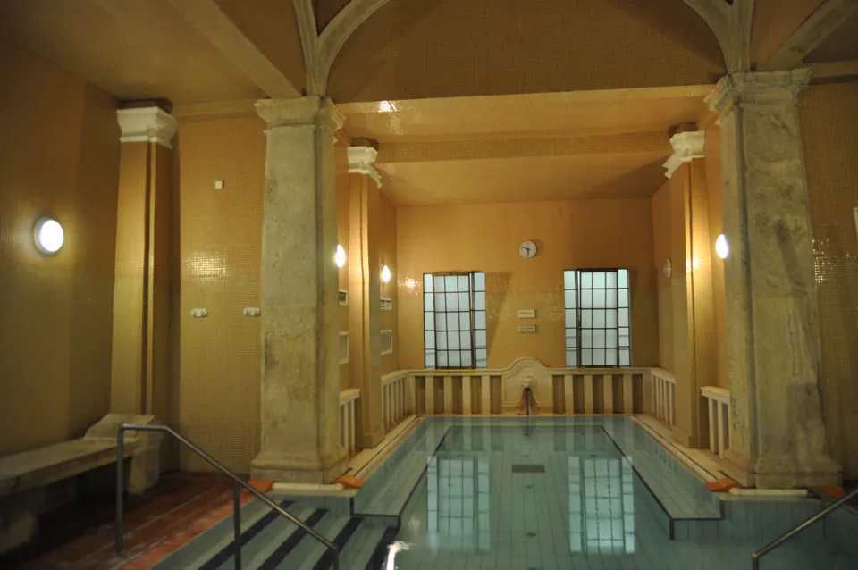 Historic indoor thermal pool with stone columns and arched ceiling in warm lighting