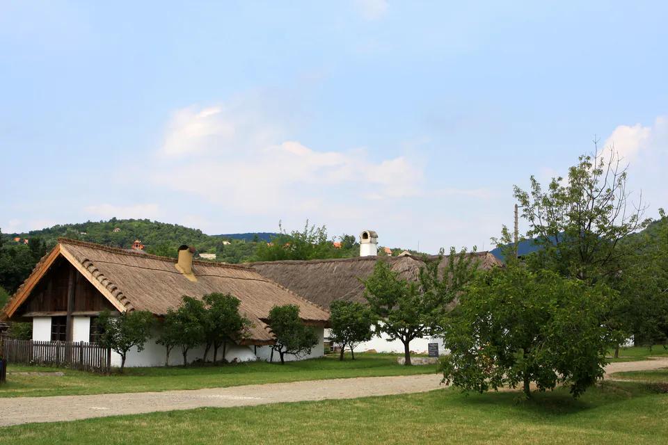 Traditional Hungarian farmhouse with thatched roof and white walls in open-air museum landscape