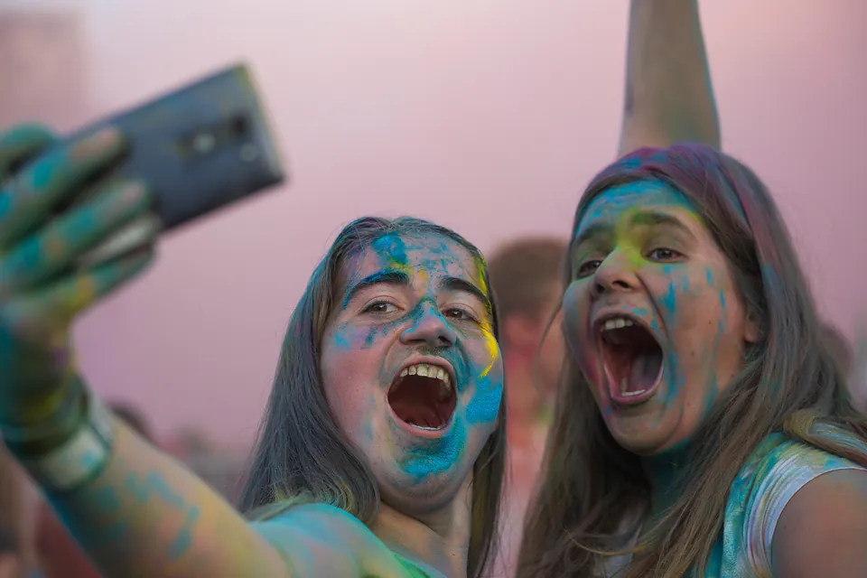 Festival-goers with colorful paint on their faces taking a selfie at sunset