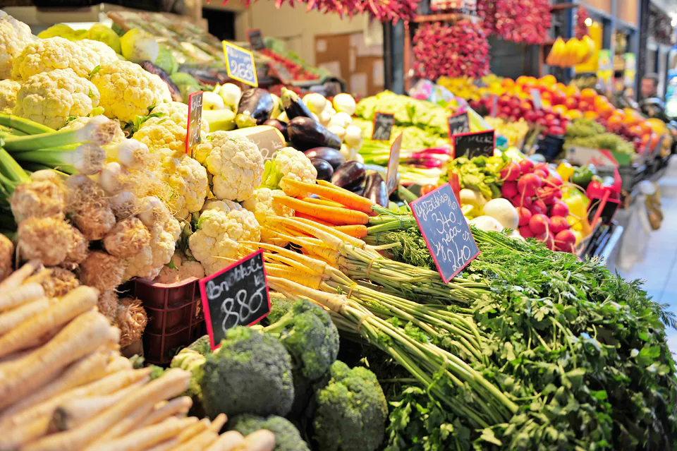 Fresh produce display at market with colorful vegetables, herbs and price tags