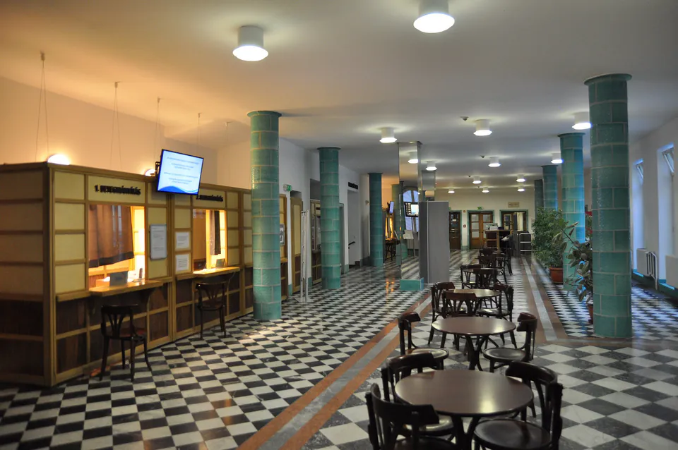 Interior lobby of Lukács Bath showing ticket windows, checkerboard floor, and green columns