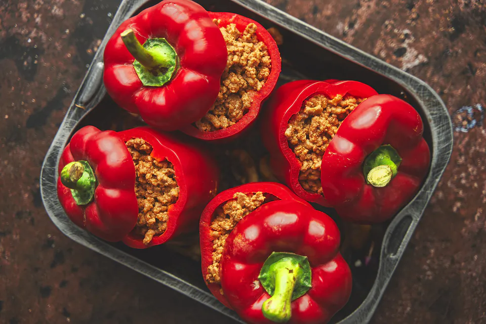 Red bell peppers stuffed with seasoned meat and rice filling in a dark baking dish