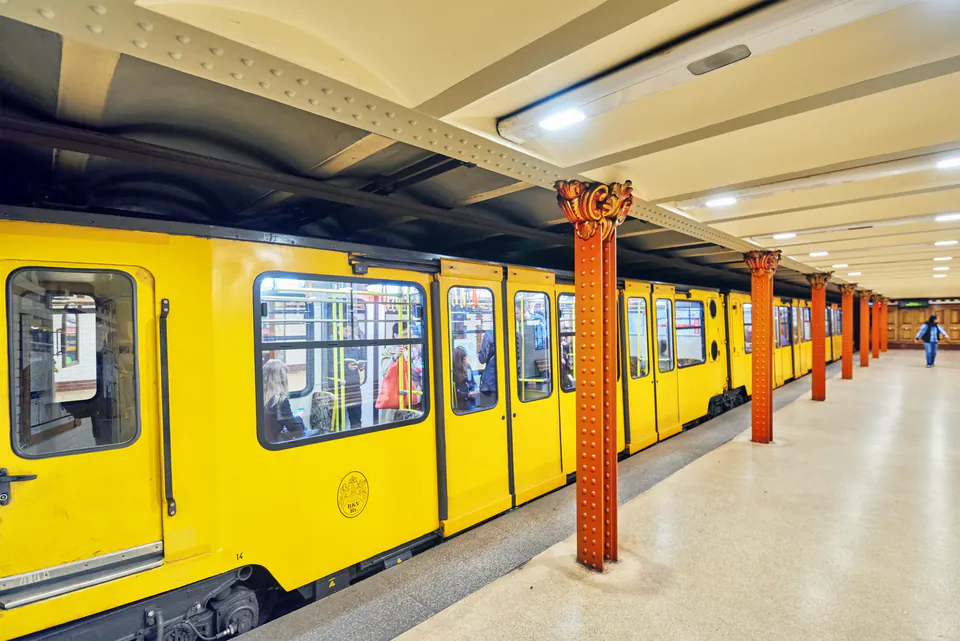 Historic yellow M1 metro train stationed at platform with ornate red columns and vaulted ceiling